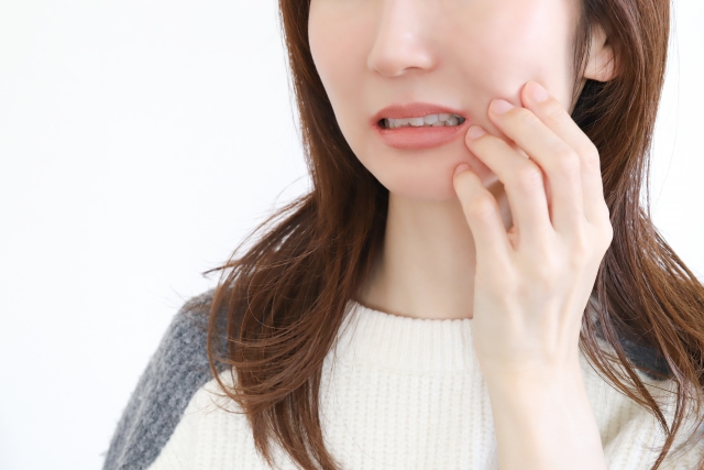 虫歯を手で押さえている女性の画像